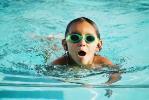 Boy swimming in a pool with his head up.